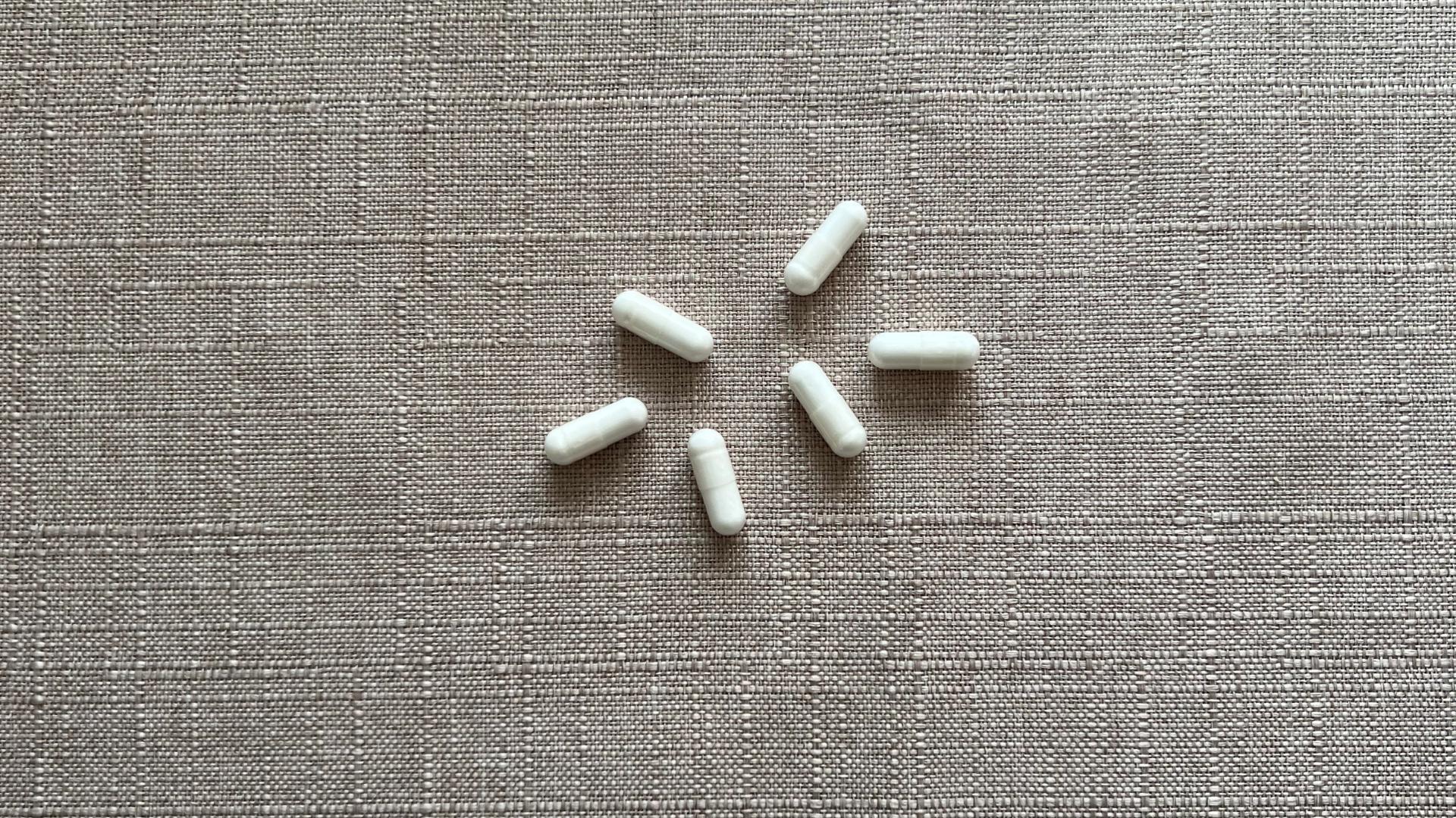 Six nondescript capsules against a neutral background representing the size and shape of common probiotic supplements